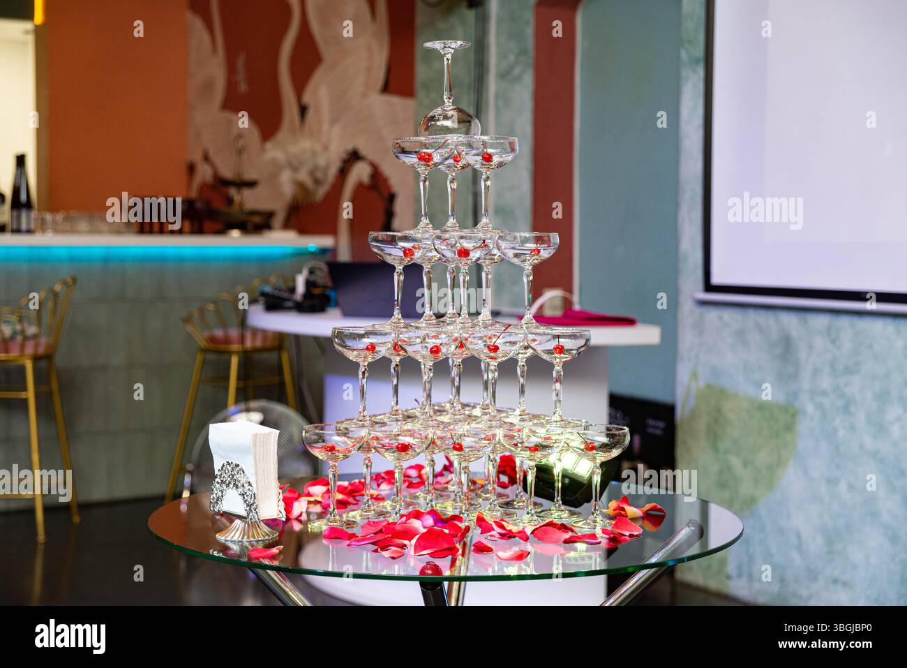 Elegante Pyramide aus Coupé-Sektgläsern mit Kirschen, umgeben von Rosenblättern, für eine stilvolle Feier oder Veranstaltung. Stockfoto