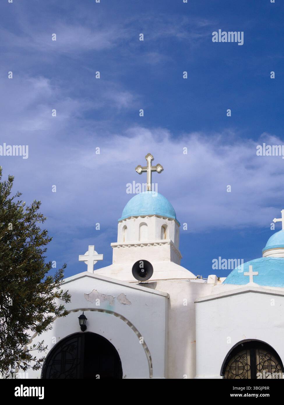 Weiße griechische Kapelle mit blauer Kuppel auf dem Lycabettus-Hügel in Athen, vom öffentlichen Weg aus gesehen. Klarer Himmel, umrahmt von Ästen. Stockfoto