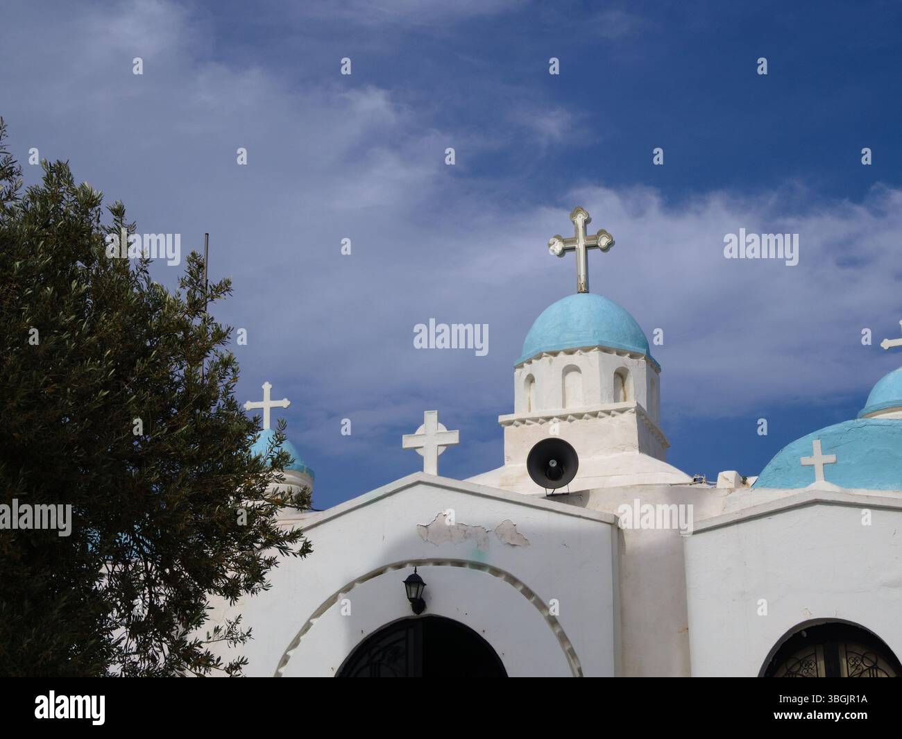 Weiße griechische Kapelle mit blauer Kuppel auf dem Lycabettus-Hügel in Athen, vom öffentlichen Weg aus gesehen, eingerahmt von Ästen. Stockfoto