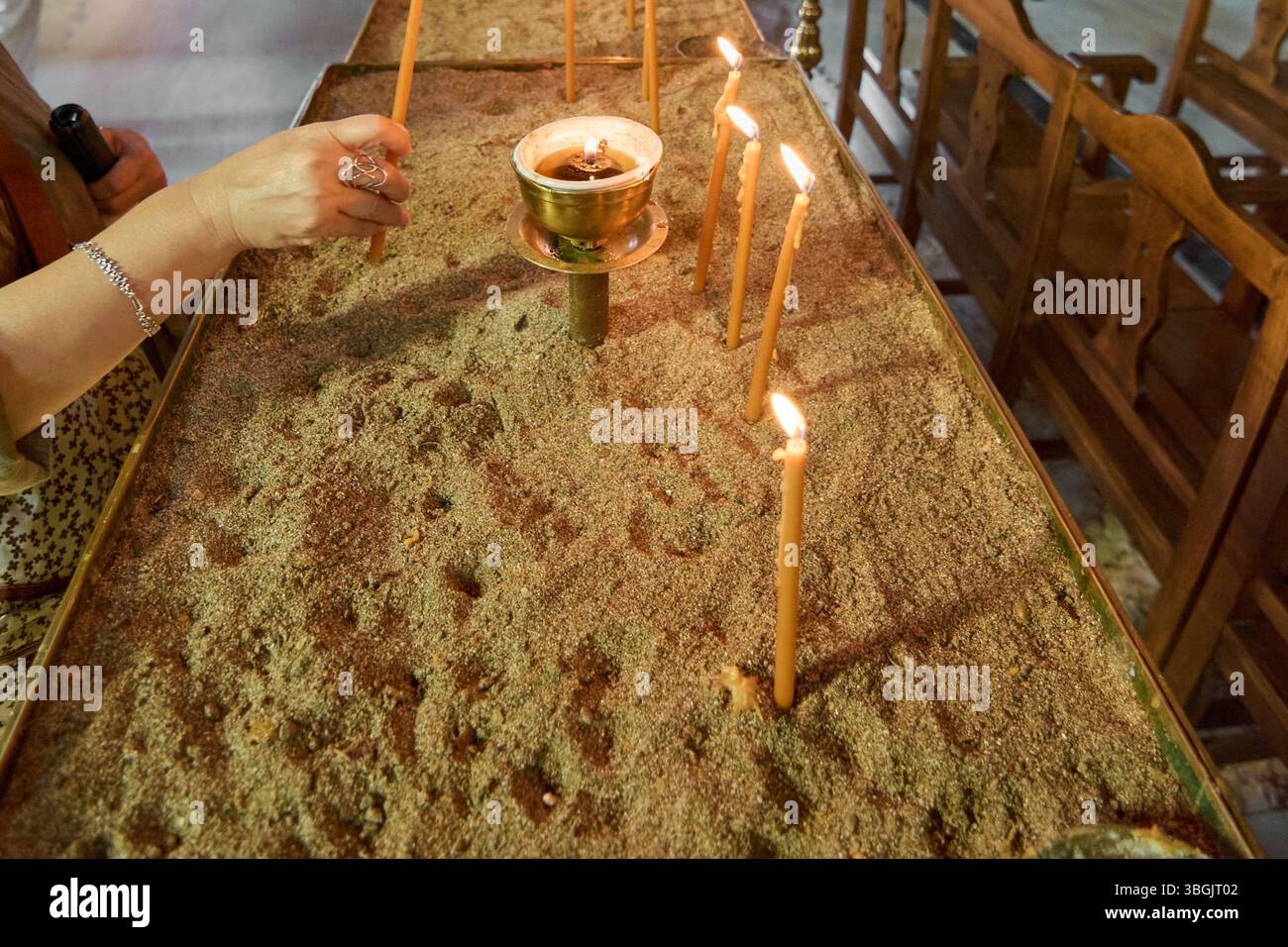 Eine Hand, die eine Kerze in der Verkündigungskirche zündet, ein symbolischer Akt des Gebets und der spirituellen Verehrung, mit Reihen von Holzbänken im Hintergrund Stockfoto