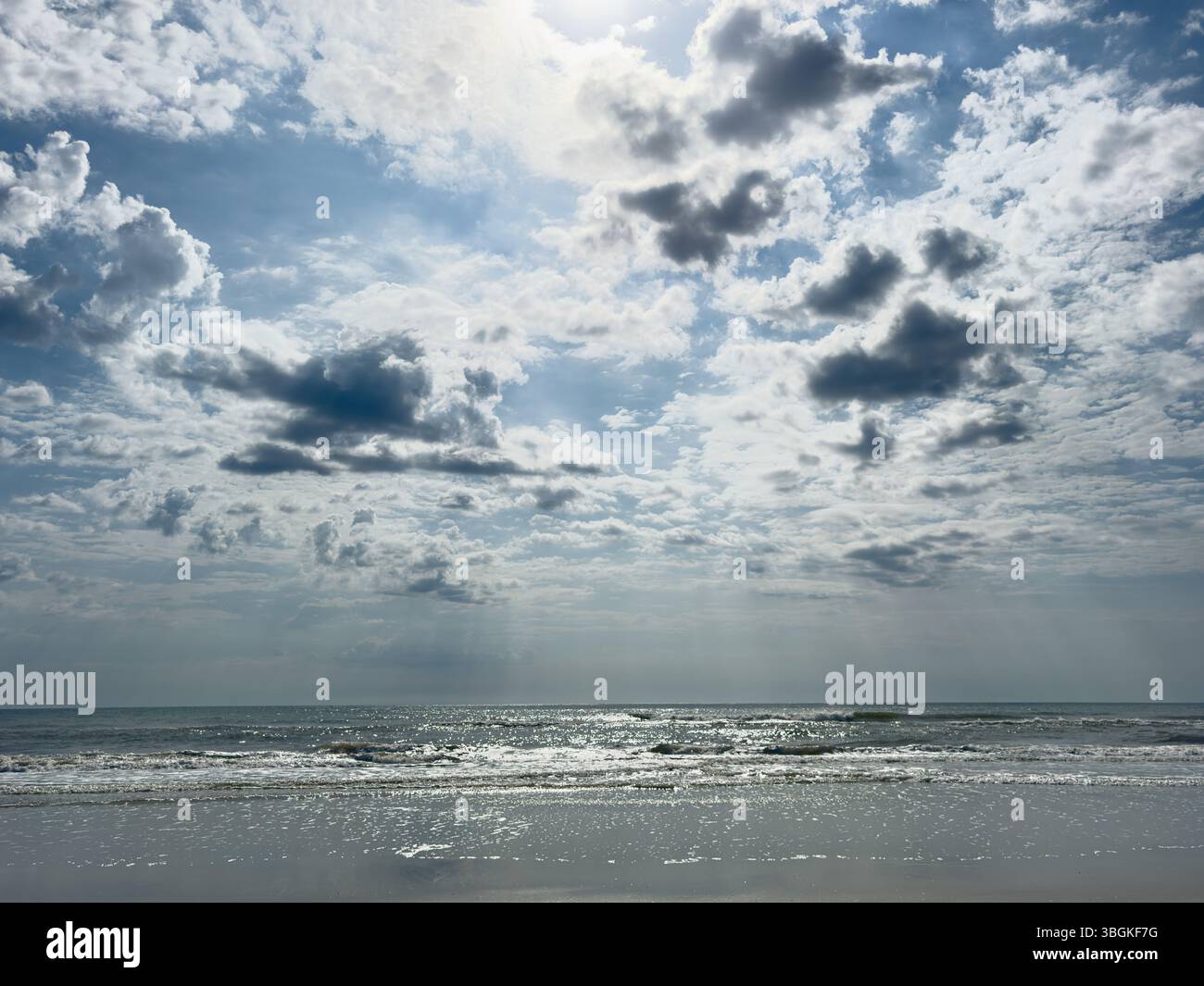 Eine kraftvolle Mittagsszene mit Sonnenlicht, das durch dramatische Wolken über einer ruhigen Meeresküste durchdringt. Dieses hochauflösende Bild erfasst die Kontrastmittel-BE - Smartphone-aufgenommenes Stockfoto