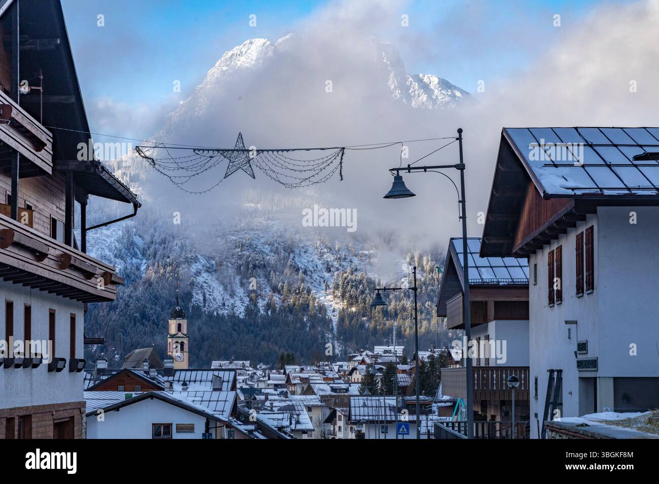 Winterszene in Sappada säumen alpine Häuser und Geschäfte die Hauptstraße mit einem Dolomitengipfel im Hintergrund, Provinz Udine, Dolomiten, Italien Stockfoto