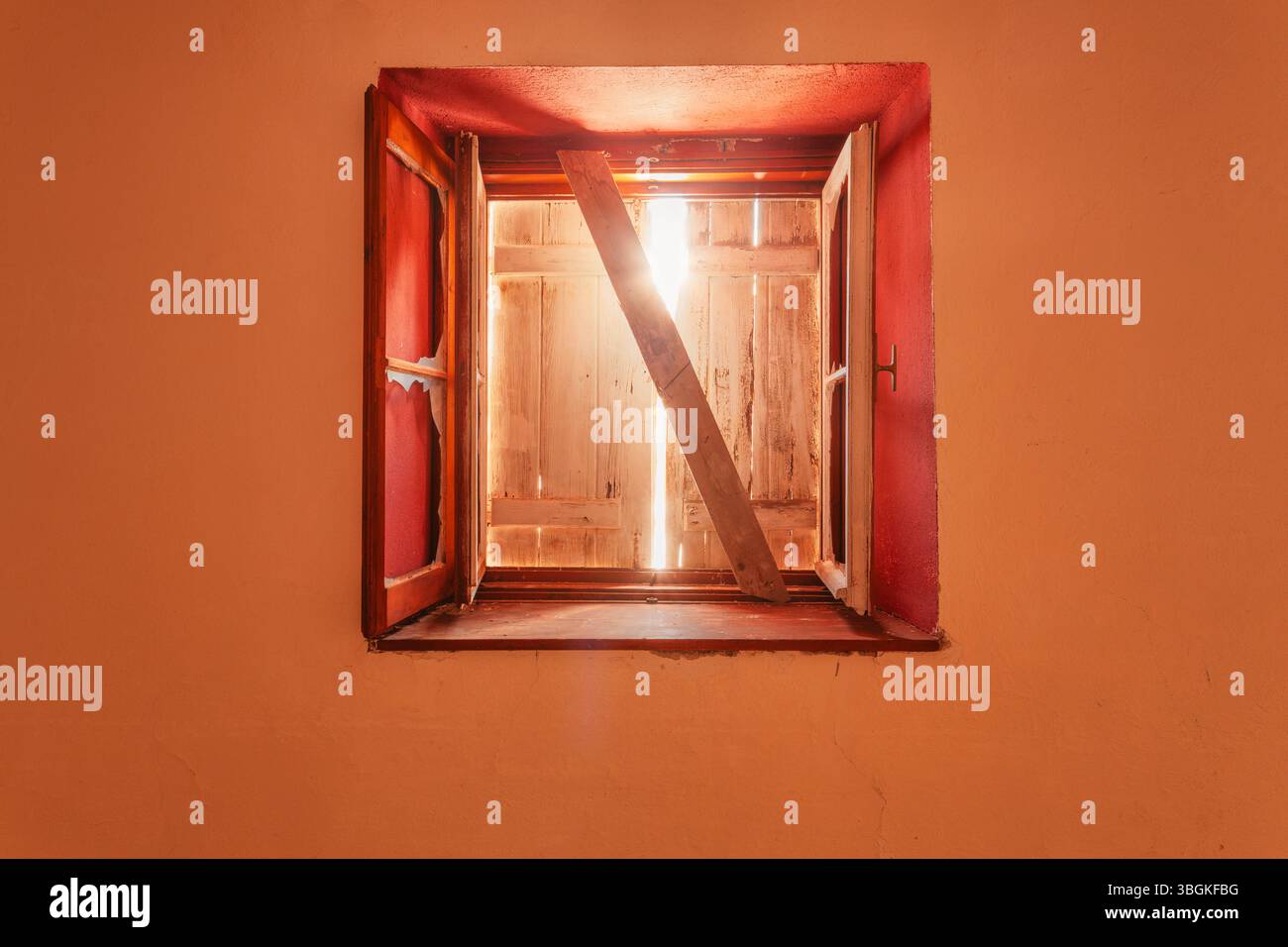 Altes rotes Fenster mit Rollenverschluss auf verlassenem alpinen Gebäude, mit gefiltertem Licht durch Holzrisse Stockfoto