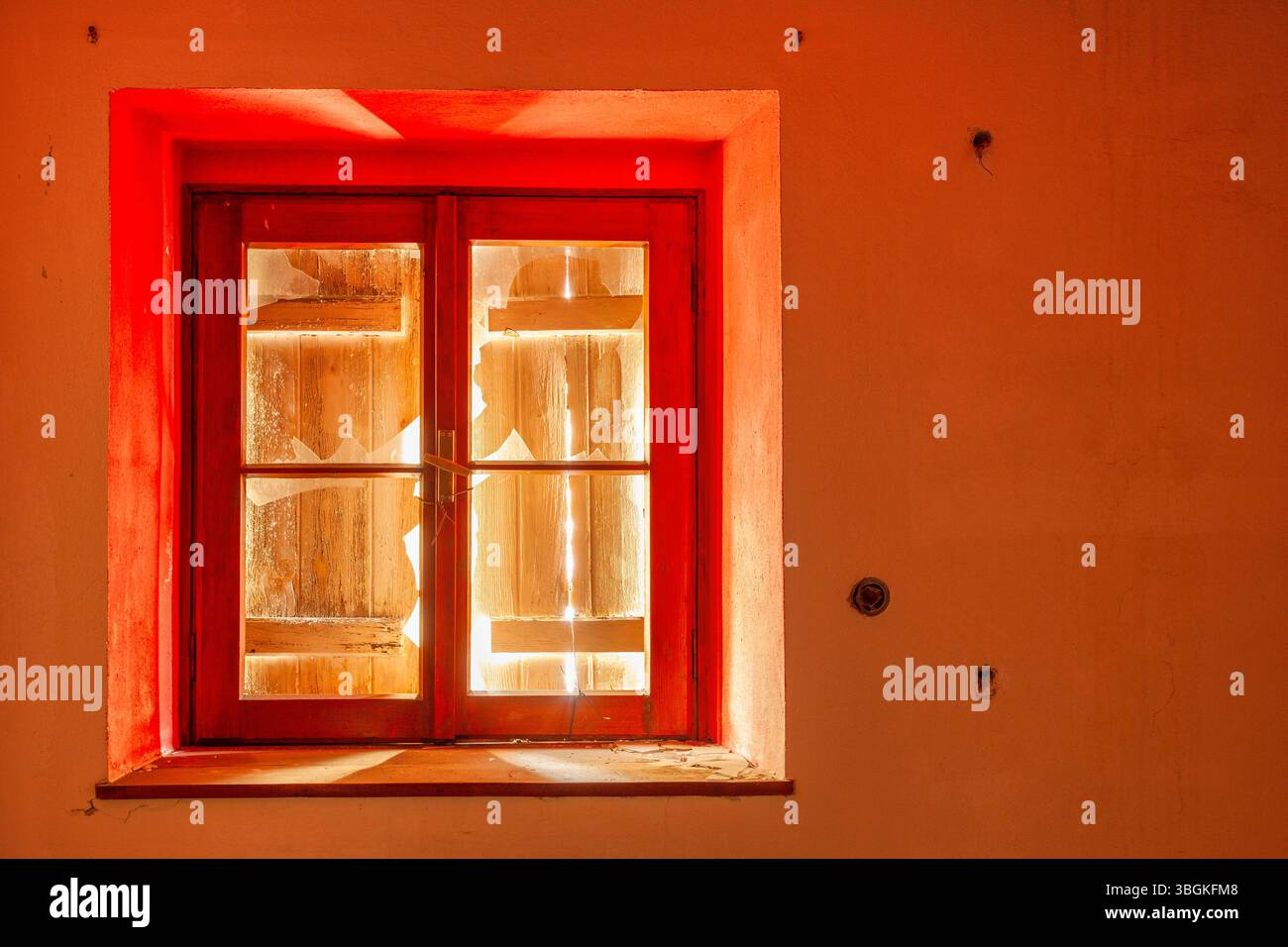 Altes rotes Fenster mit Rollenverschluss auf verlassenem alpinen Gebäude, mit gefiltertem Licht durch Holzrisse Stockfoto