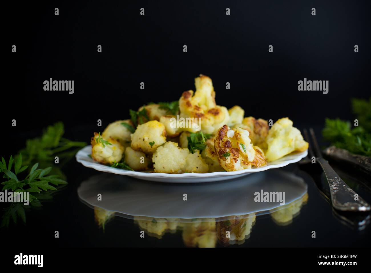 Gebratener Blumenkohl mit Gewürzen und Kräutern auf schwarzem Hintergrund. Stockfoto