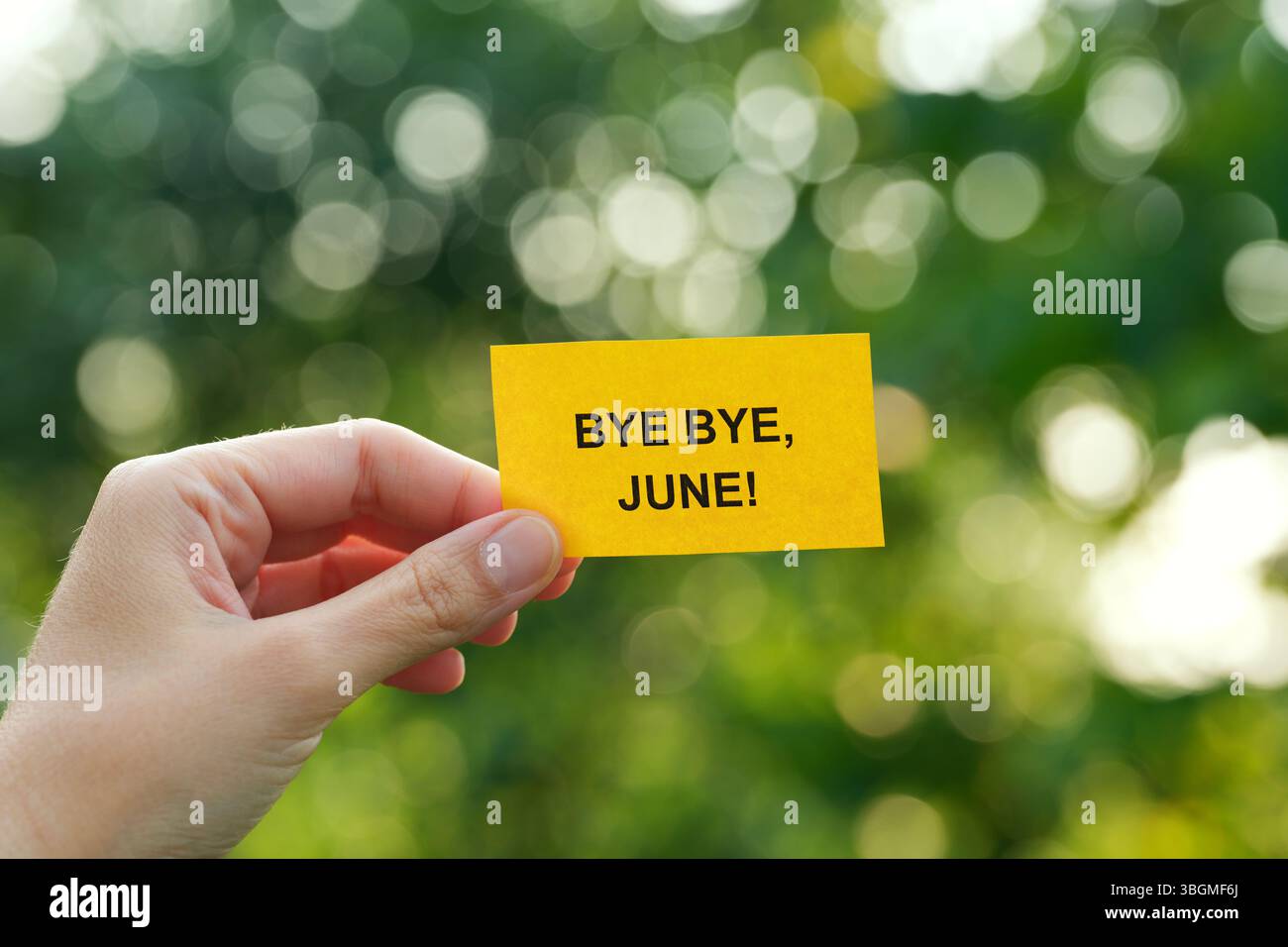 Eine Frau, die ein gelbes Stück Papier hält, mit den Worten Bye Bye, June! Auf ihr in der Hand vor einem Laubhintergrund. Nahaufnahme. Stockfoto