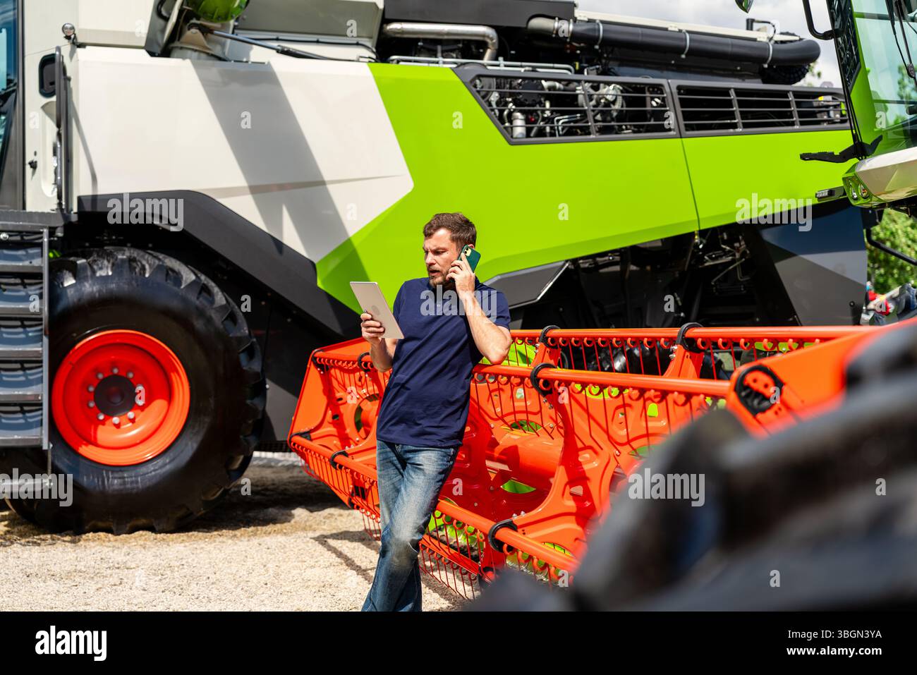 Mitarbeiter in der Landwirtschaft, die ein Tablet verwenden und auf dem Mobiltelefon in der Nähe des Traktors sprechen Stockfoto