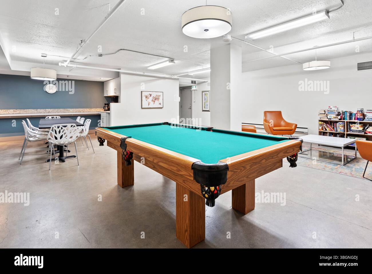 Billardtisch steht in einem Zimmer mit ein paar Stühlen und einer Couch. Das Zimmer ist größtenteils weiß und hat eine blaue Wand Stockfoto