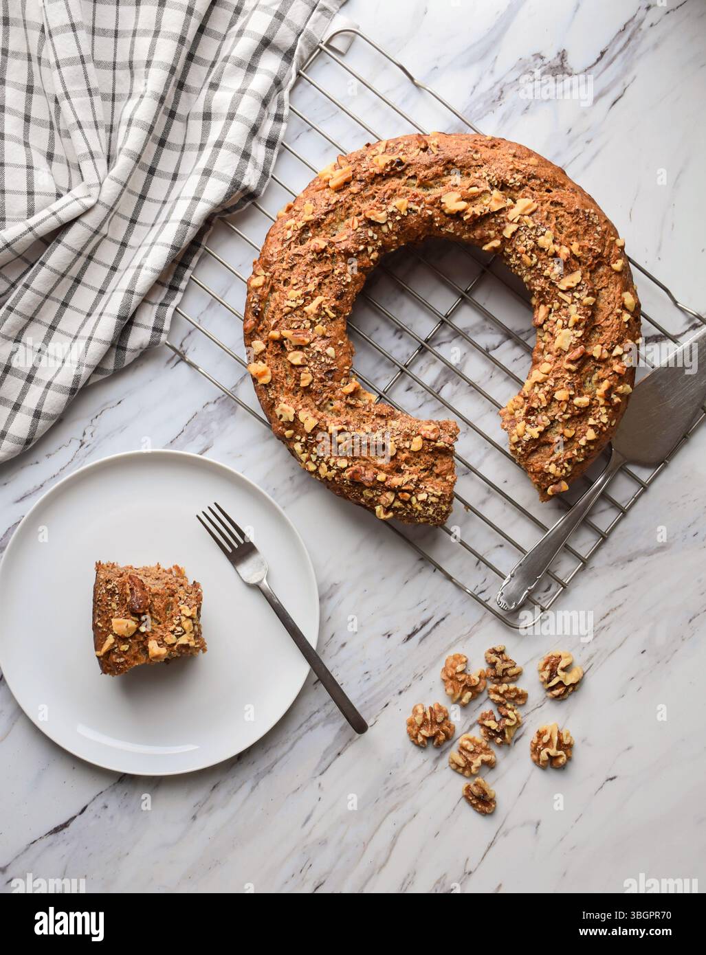 Ansicht von oben nach unten: Kuchenbündel mit Walnüssen, die auf einem Gestell mit einer Scheibe auf einem Teller auf einer Marmoroberfläche gekühlt werden Stockfoto