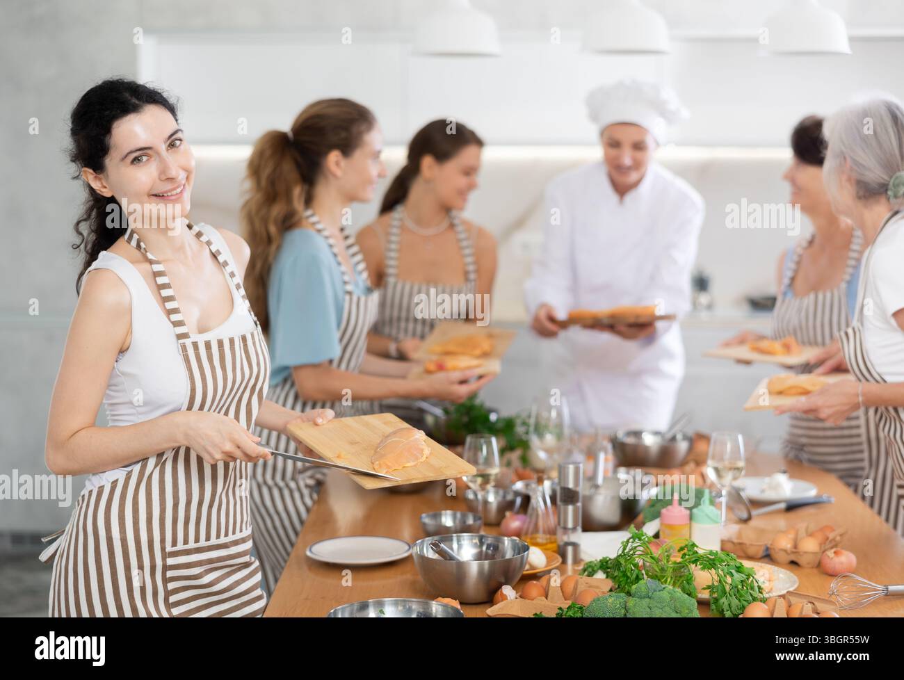 Mädchen in der Kochschule schneidet Hühnchen und bereitet kalorienarmes Mittagessen zu Stockfoto