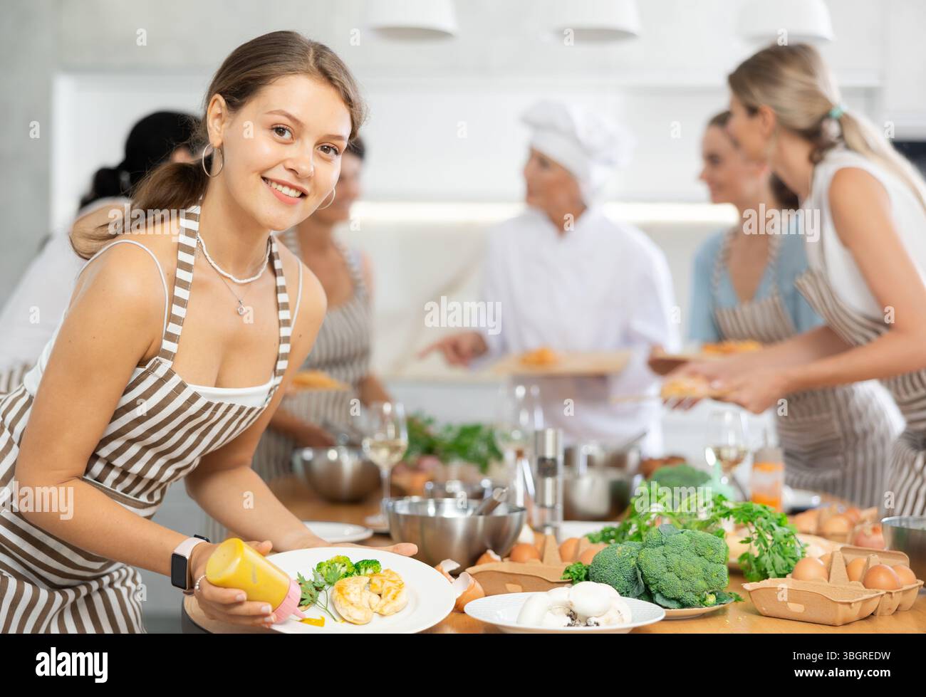 Mädchen, die die kulinarische Schule besuchen, schmücken fertiges Gericht, gebratenes Hähnchenfilet mit goldener Kruste. Stockfoto