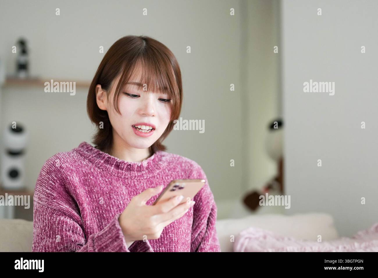 In einem sauberen, einfachen Raum mit sanftem Licht trägt eine schwangere Japanerin Anfang 20 mit kurzen braunen Haaren ein rosafarbenes Strickkleid. Sie sitzt auf einem Stockfoto