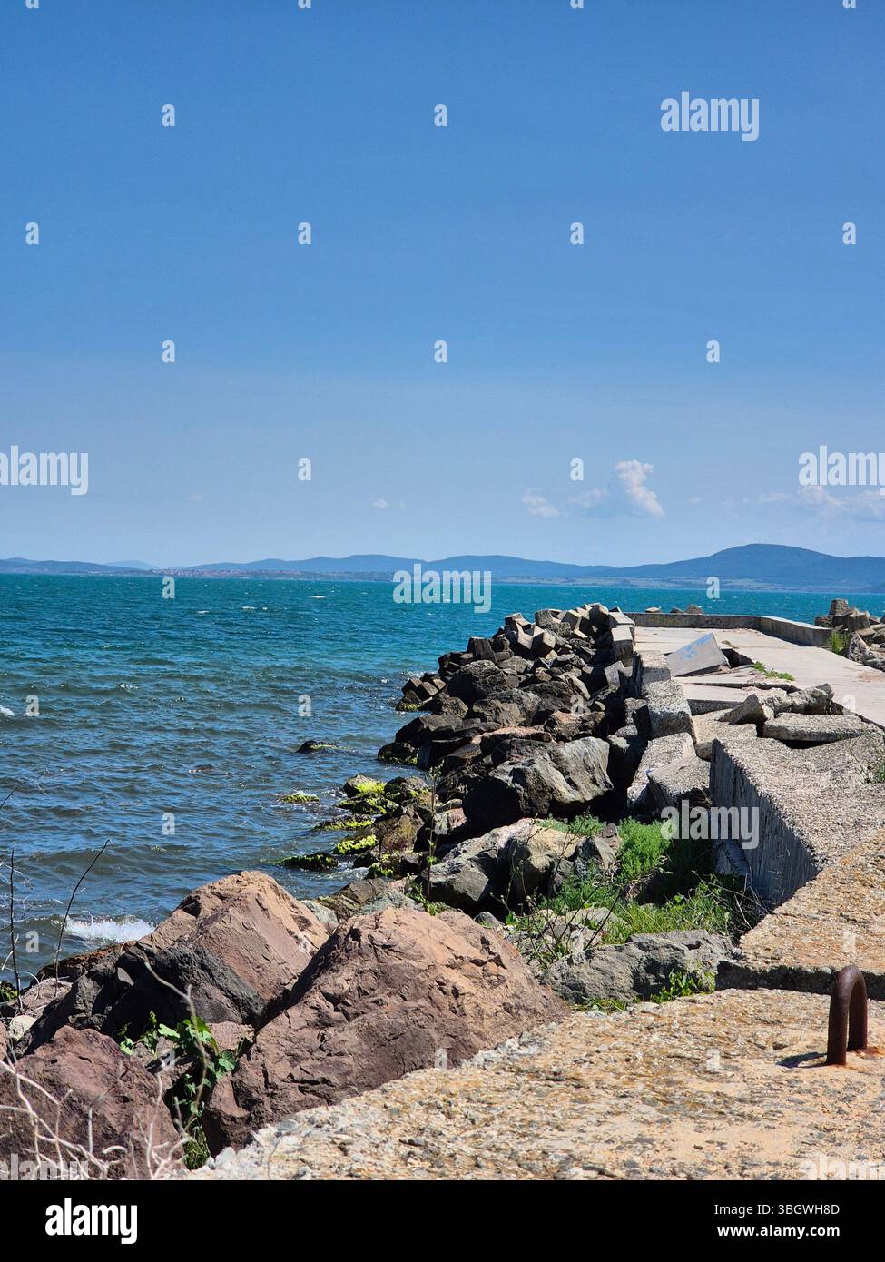 Wellenbrecher, die sich bis ins Meer erstrecken. Betonpier, felsiger Kamm im Meer. Sonniger Tag. Sommer - Smartphone-aufgenommenes Stockfoto