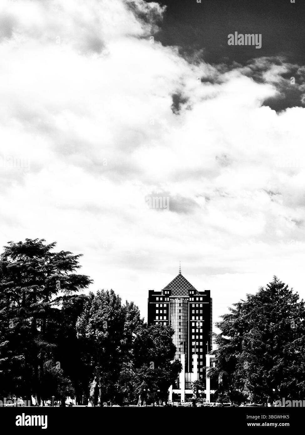 Schwarzweißfoto. Ein hohes Gebäude mit einem unverwechselbaren Dach, das von Bäumen eingerahmt wird, vor einem bewölkten Himmel Stockfoto