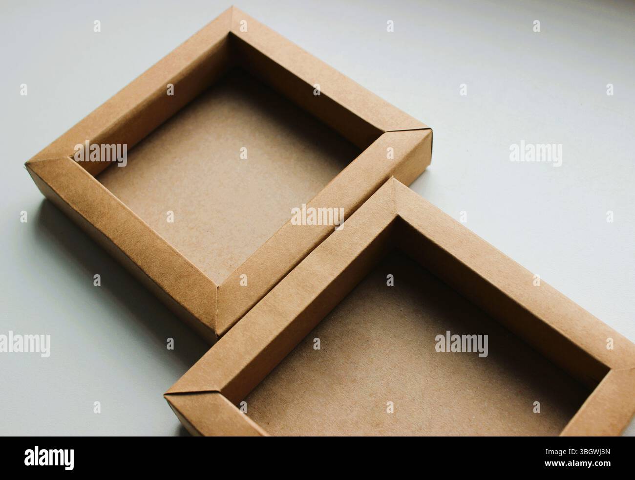 Zwei quadratische Pappschalen, die auf einem weißen Tisch miteinander verbunden sind. Leere Kartonhüllen nebeneinander auf weißem Flachbild isoliert Stockfoto