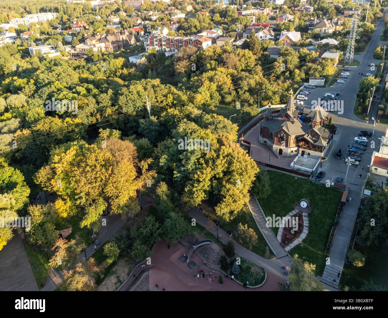 Drohnenblick auf eine Holzkirche neben einem Spielplatz in einem üppig grünen Stadtpark Stockfoto