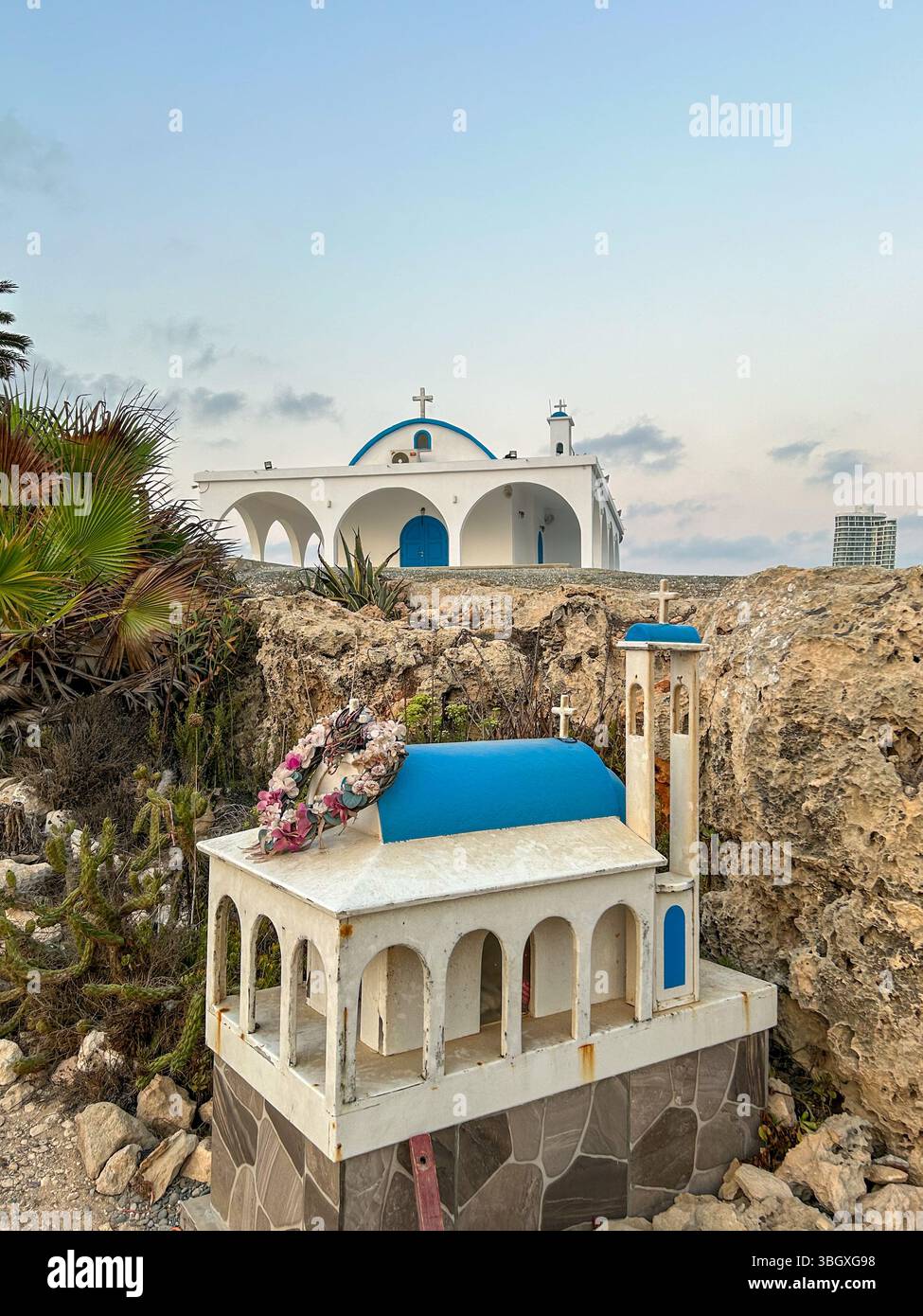 Malerischer Blick auf die St. Thekla Kirche in Ayia Napa, Zypern, mit einem kleinen Schrein am Straßenrand im Vordergrund und der ikonischen weiß-blauen Architektur im Th Stockfoto