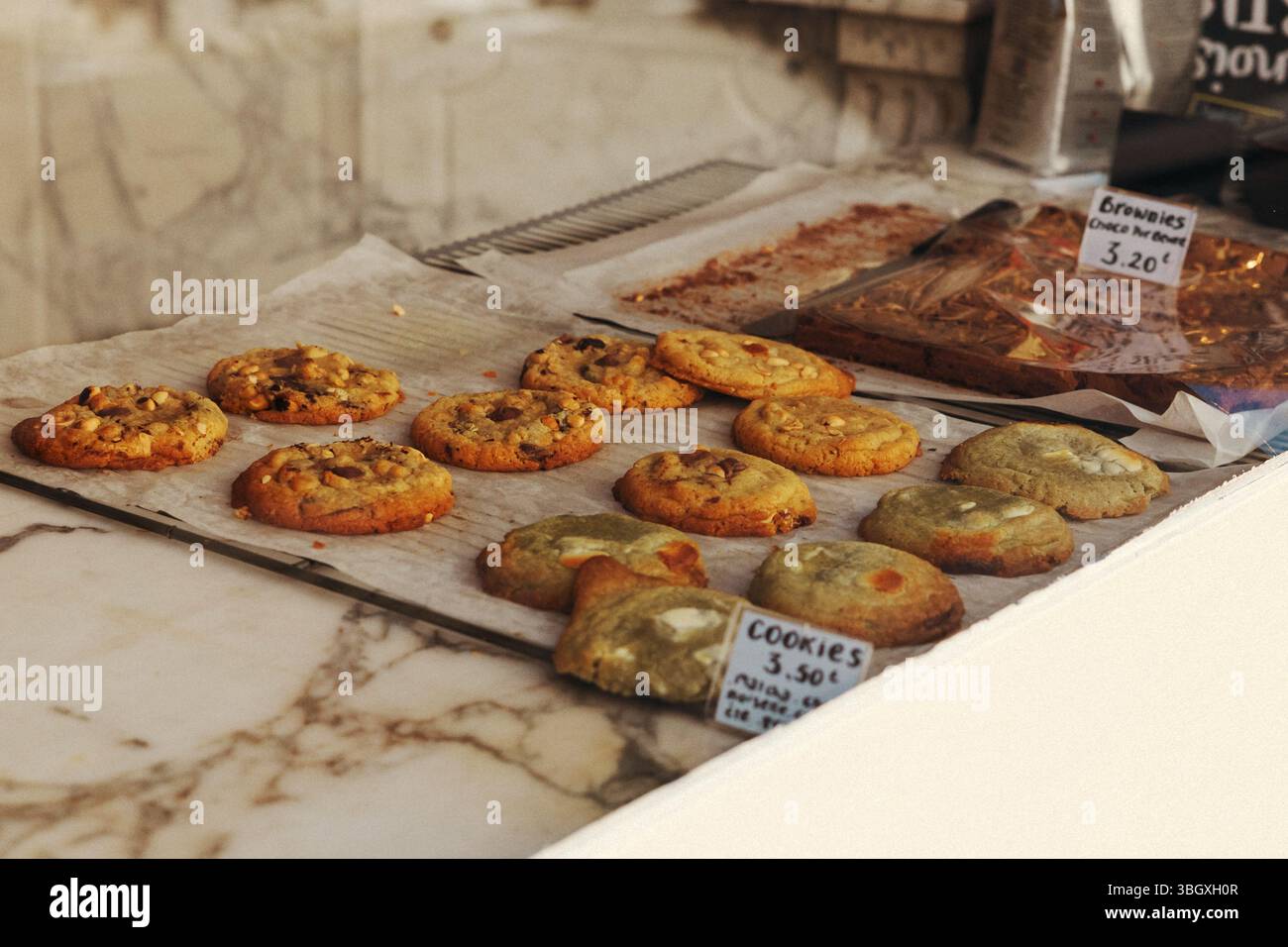 Eine verlockende Präsentation verschiedener frisch gebackener Plätzchen und Brownies auf Pergamentpapier auf einer Marmorplatte in einer charmanten Bäckerei. Stockfoto