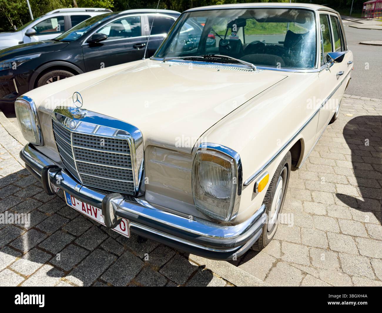 Beigefarbener Mercedes-Benz W115 Oldtimer, abgestellt in sonniger Umgebung, umgeben von anderen Fahrzeugen Stockfoto