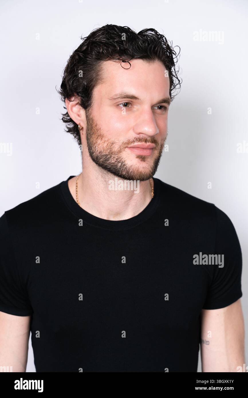 Ein Porträt eines jungen Mannes mit dunklen lockigen Haaren, einem Stoppelbart und einem goldenen Ohrring, der ein schwarzes T-Shirt und eine goldene Kette trägt. Er schaut auf Th Stockfoto