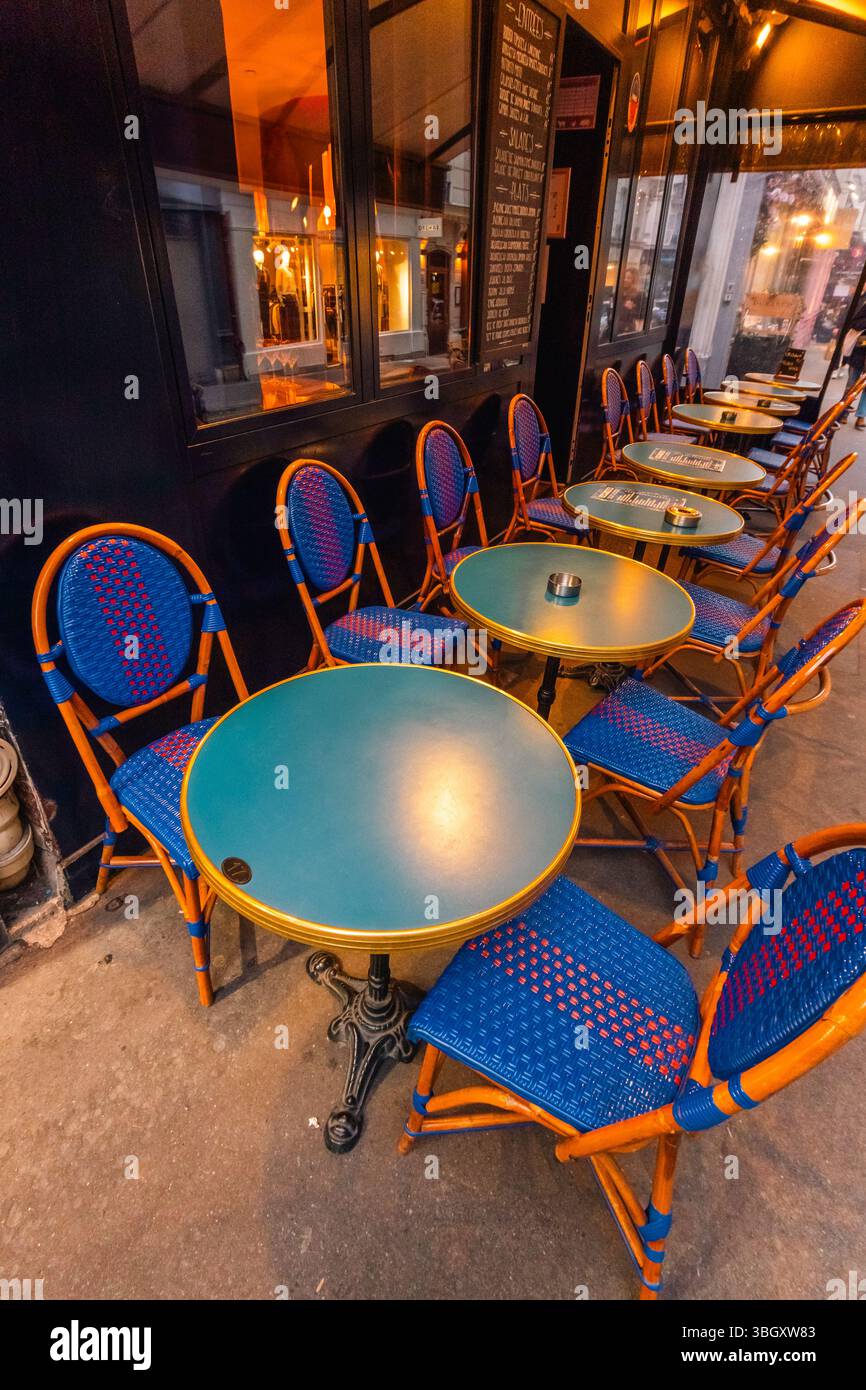 Abends stehen auf der Außenterrasse eines Pariser Cafés in hellen Farben in Blau und Orange gewebte Bistrostühle um runde Metalltische. Krieg Stockfoto