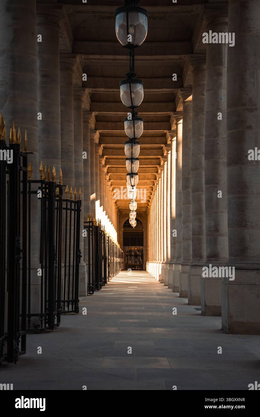 : Eine lange, symmetrische Perspektive durch die historische Kolonnade des Palais-Royal in Paris, wo sich wiederholende Säulen und hängende Laternen ein d Stockfoto