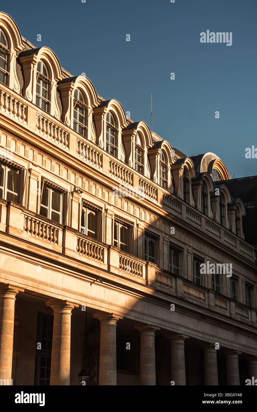 Die obere Fassade eines kunstvoll verzierten Pariser Gebäudes mit Reihen von bogenförmigen Fenstern und klassischen Säulen, die in das warme Licht der Einrichtung getaucht sind Stockfoto