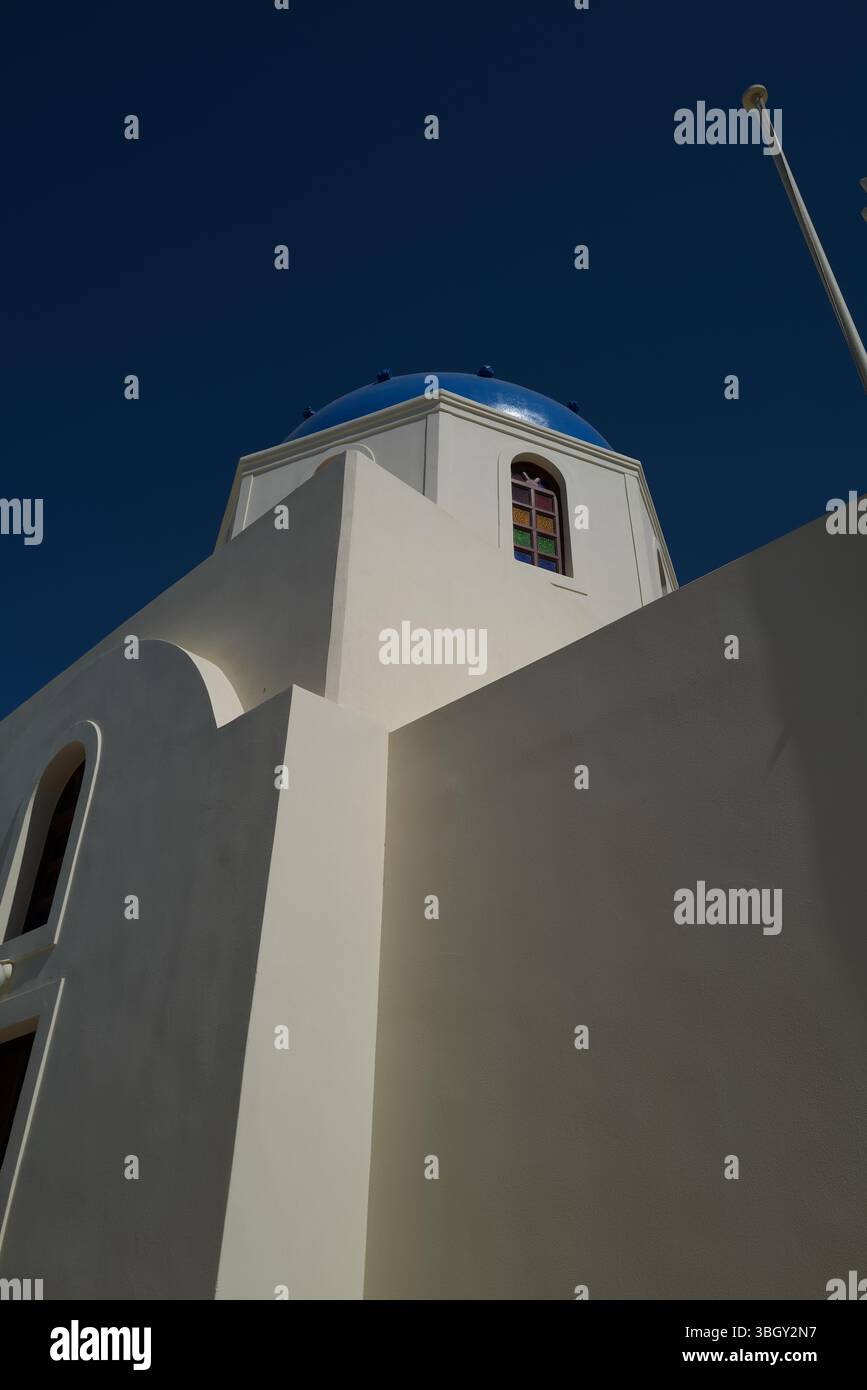 Eine klassische weiß getünchte Kirche mit einer blauen Kuppel und einem farbenfrohen Fenster unter dem tiefblauen Himmel von Santorin, die die ikonische Architektur der Insel einfängt Stockfoto
