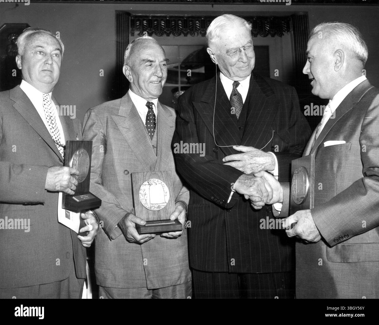 Bernard Baruch, der 1956 Preisträgern den Horatio Alger Award verliehen hat, schüttelt bei den Waldorf Astoria-Zeremonien die Hand mit Armando Conti (rechts), Präsident der Trenton Beverage Company. Gewinner waren Roy T Hurley (links), Präsident der Curtiss Wright Corporation und Edward „Eddie“ V Rickenbacker, Präsident der Eastern Airlines. 10. Mai 1956 Stockfoto