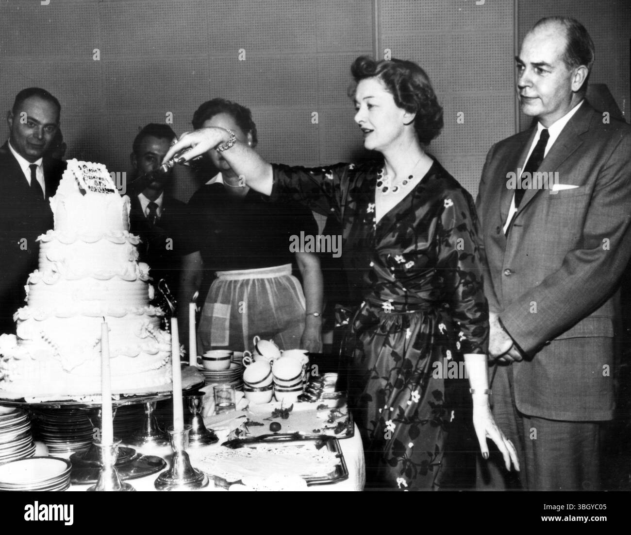 Während ihr Ehemann Howland H. Sargent (rechts) zusieht, schneidet die Schauspielerin Myrna Loy den Kuchen auf einer Geburtstagsfeier zum 5. Jahrestag der Radio Liberation in den New York City Studios. 6. März 1958 Stockfoto Während ihr Ehemann Howland H. Sargent (rechts) zusieht, schneidet die Schauspielerin Myrna Loy den Kuchen auf einer Geburtstagsfeier zum 5. Jahrestag der Radio Liberation in den New York City Studios. 6. März 1958 Stockfoto