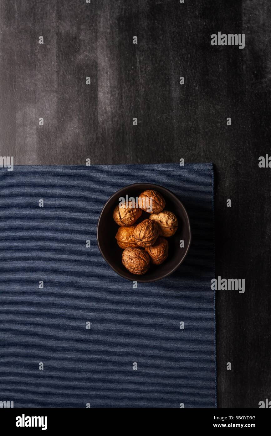 Schwarze Schüssel mit Walnüssen und blauem Tischtuch auf schwarzem Tafel Hintergrund. Flache Lagen. Draufsicht. Stockfoto