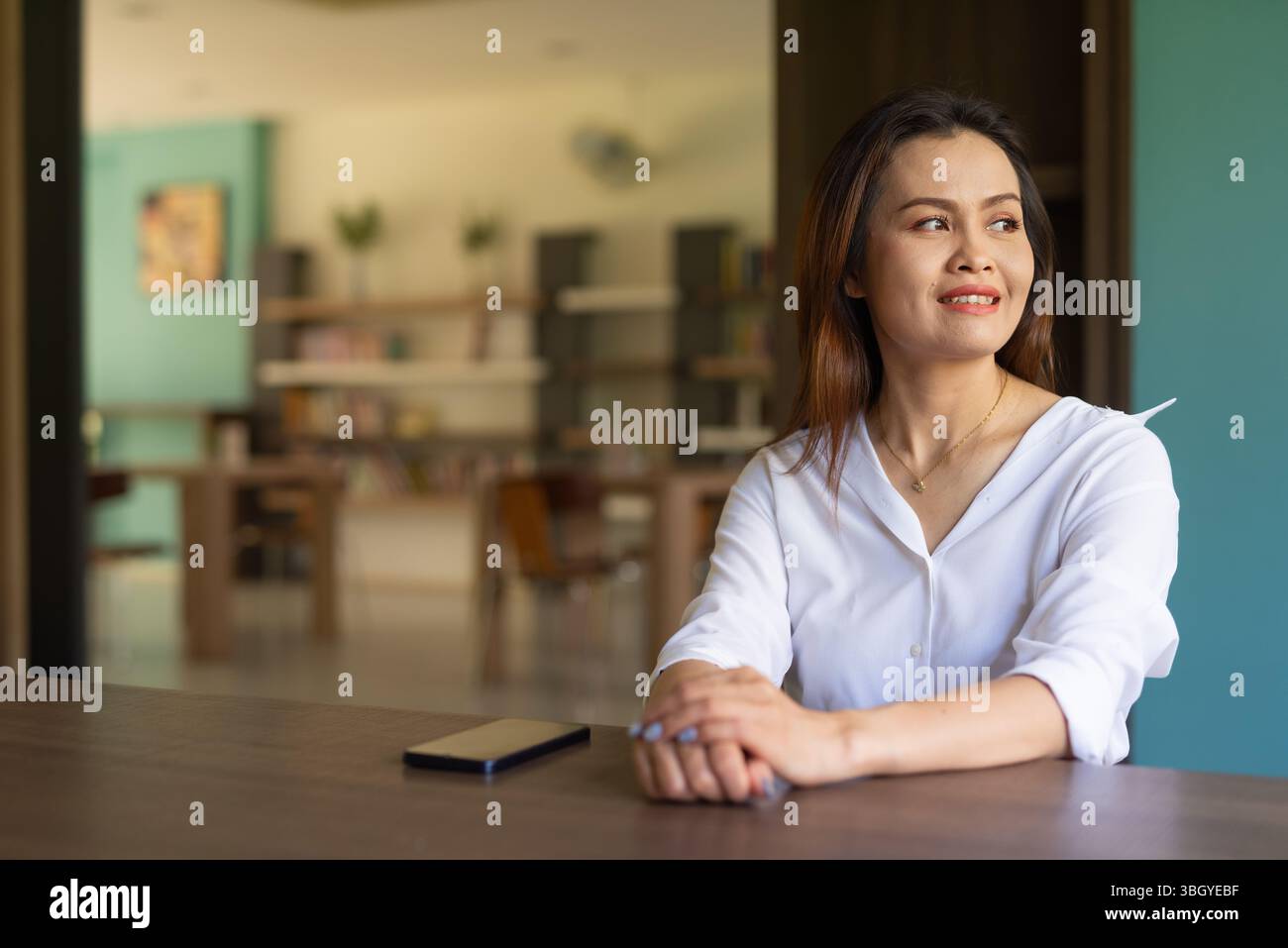 Porträt einer schönen asiatischen Frau, die in der Bibliothek sitzt Stockfoto