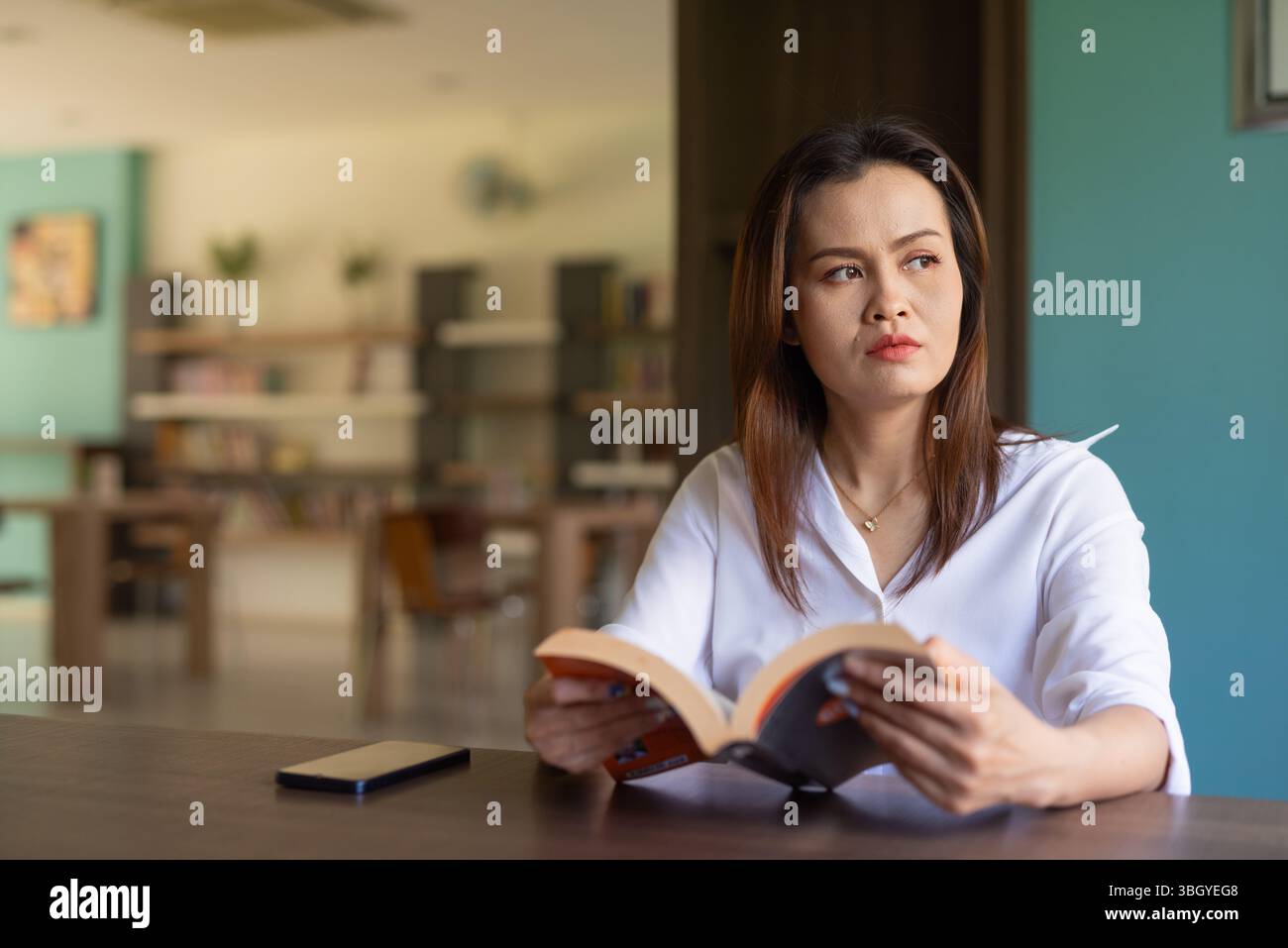 Porträt einer schönen asiatischen Frau, die in der Bibliothek sitzt Stockfoto
