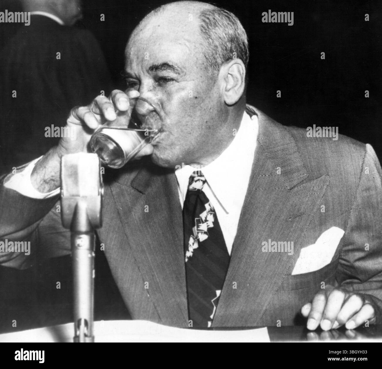 Grunewald spricht mit Hausforschern. Henry W Grunewald, der mysteriöse Mann von Washington, sitzt während einer Pause in seiner Aussage ein Glas Wasser, bevor der Unterausschuss des Hauses Way and Means die Steuerskandale untersucht. 13. April 1953 Stockfoto