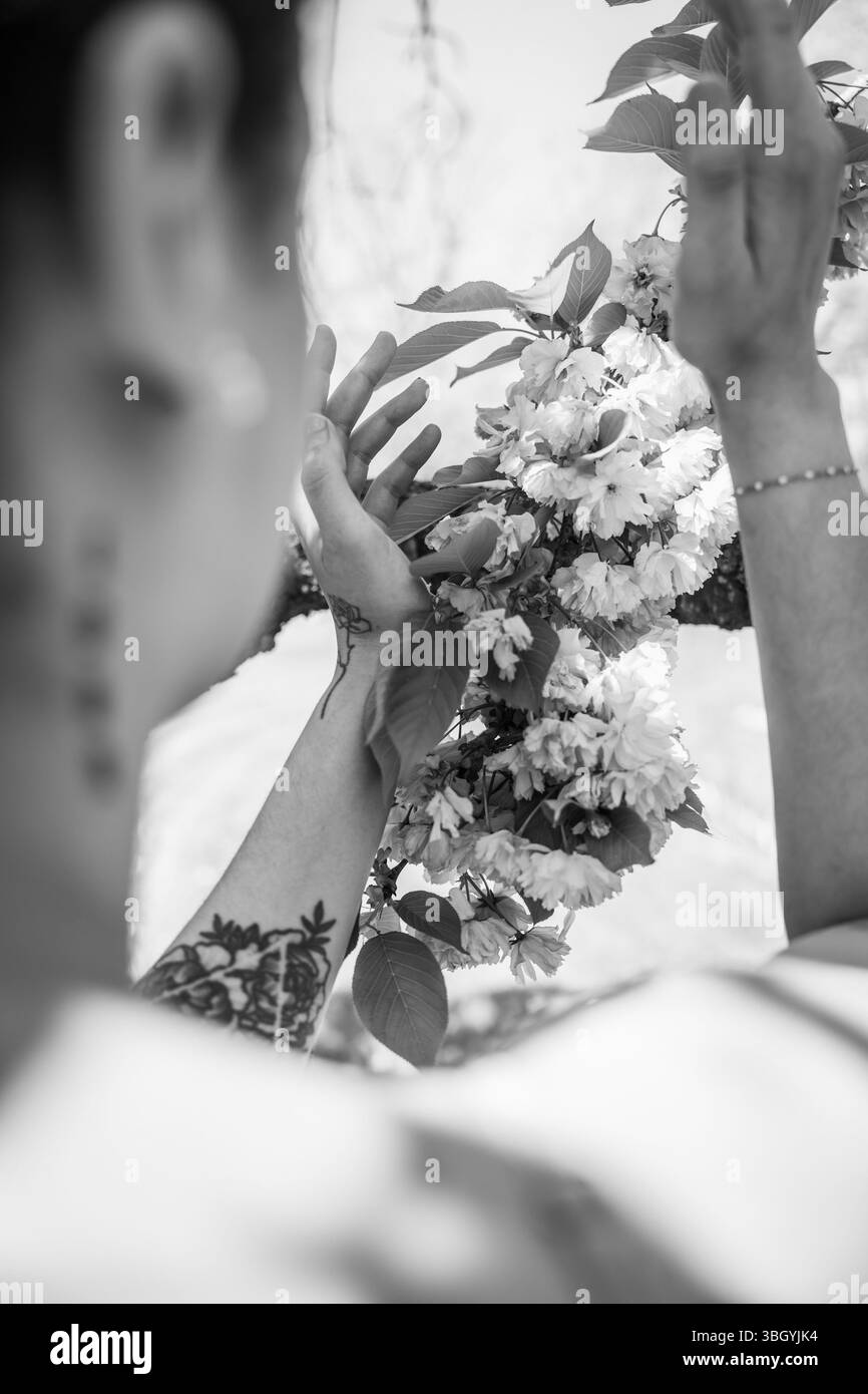 Tätowierte Arme, die in Schwarz-weiß zu blühenden Blumen reichen Stockfoto