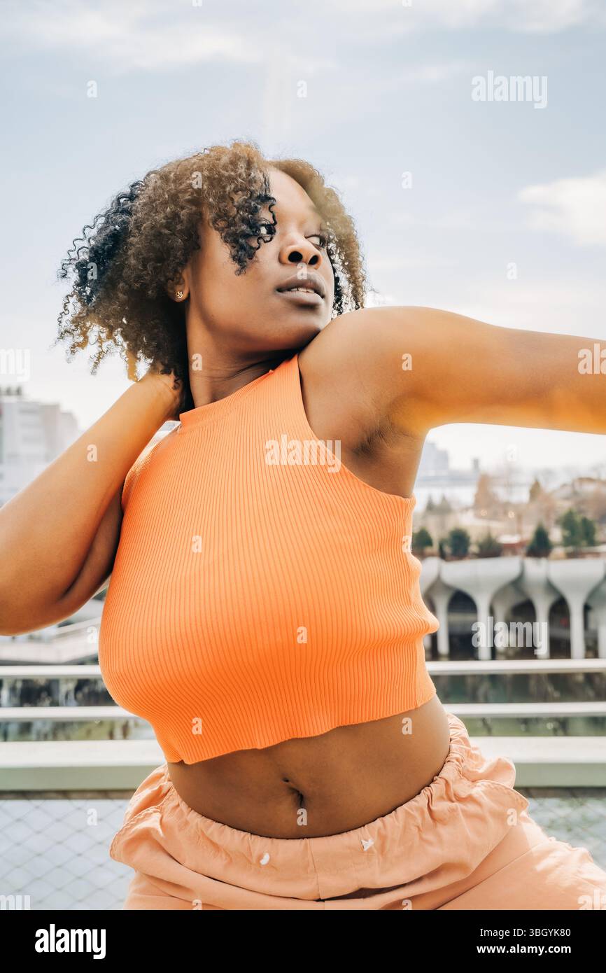 Nahaufnahme einer Frau in orangefarbener Spitze mit Stadtbild dahinter Stockfoto