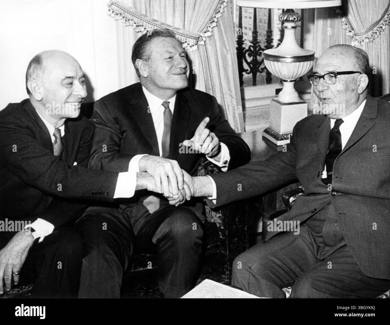 Nur noch eine. Der Gouverneur von New York Nelson Rockefeller (Mitte) erkennt die Wünsche der Fotografen für „nur einen weiteren“ an, da Louis Lefkowitz (links) als Generalstaatsanwalt von New York mit dem israelischen Premierminister Levi Eshkol während des Besuchs des Gouverneurs in der Hotelsuite von Eshkol zusammentritt. 11. Januar 1968 Stockfoto