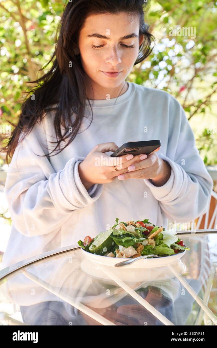 Eine Frau, die beim Mittagessen etwas auf ihrem Handy nachsieht Stockfoto