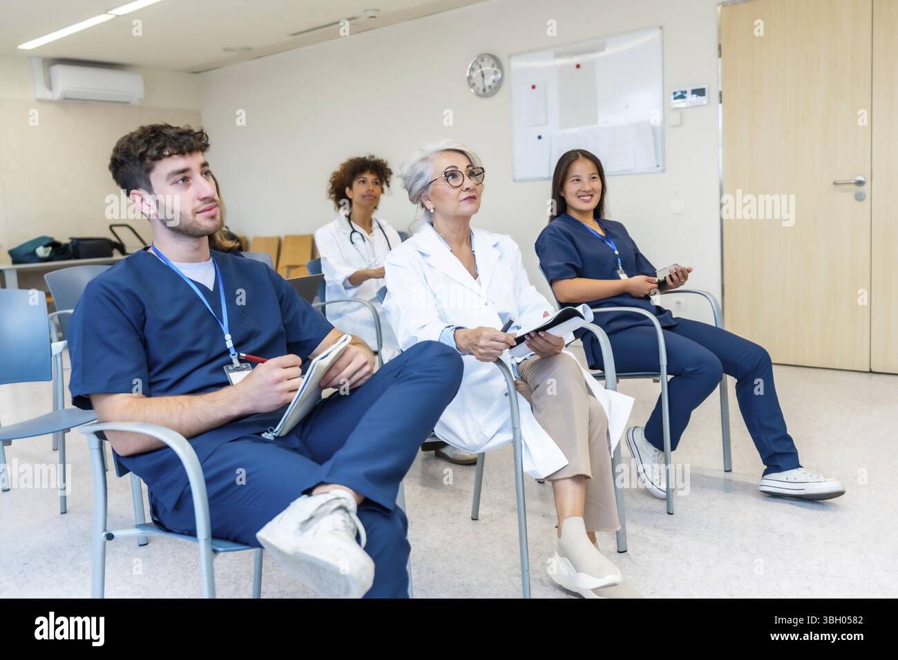 Medizinische Fachkräfte hören während einer medizinischen Konferenz aufmerksam zu, machen Notizen und erweitern ihr Wissen Stockfoto