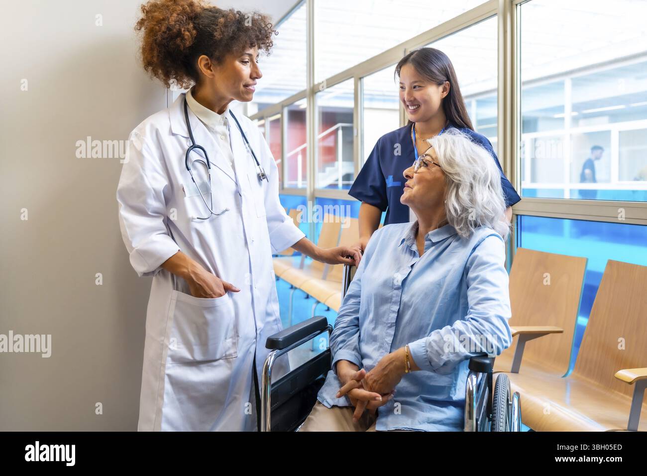 Medizinische Fachkräfte, die einen älteren Patienten im Rollstuhl betreuen und unterstützen, unterstreichen die Bedeutung der Gesundheitsversorgung für ältere Menschen Stockfoto