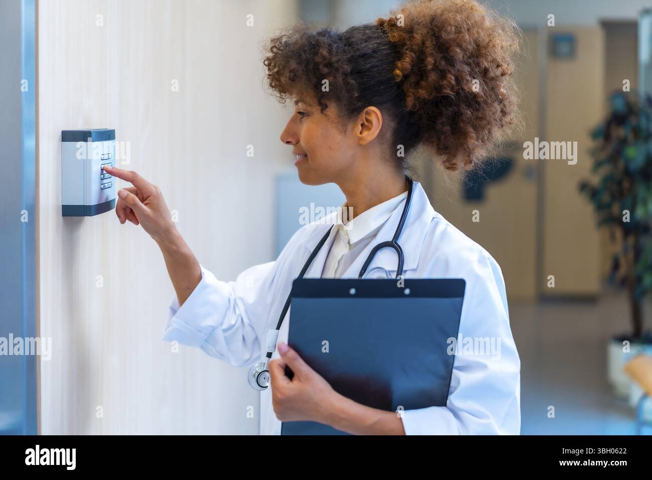 Selbstbewusste Ärztin, die einen Code über ein Tastenfeld eingibt und ein Klemmbrett in einem Krankenhausflur hält Stockfoto Selbstbewusste Ärztin, die einen Code über ein Tastenfeld eingibt und ein Klemmbrett in einem Krankenhausflur hält Stockfoto