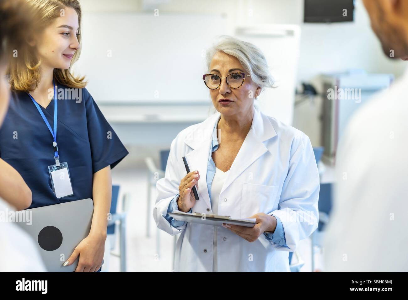 Erfahrene Ärztin, die ein medizinisches Briefing mit einem Klemmbrett und einem Stift in der Hand hält, spricht Kollegen in einem Konferenzraum des Krankenhauses an Stockfoto Erfahrene Ärztin, die ein medizinisches Briefing mit einem Klemmbrett und einem Stift in der Hand hält, spricht Kollegen in einem Konferenzraum des Krankenhauses an Stockfoto