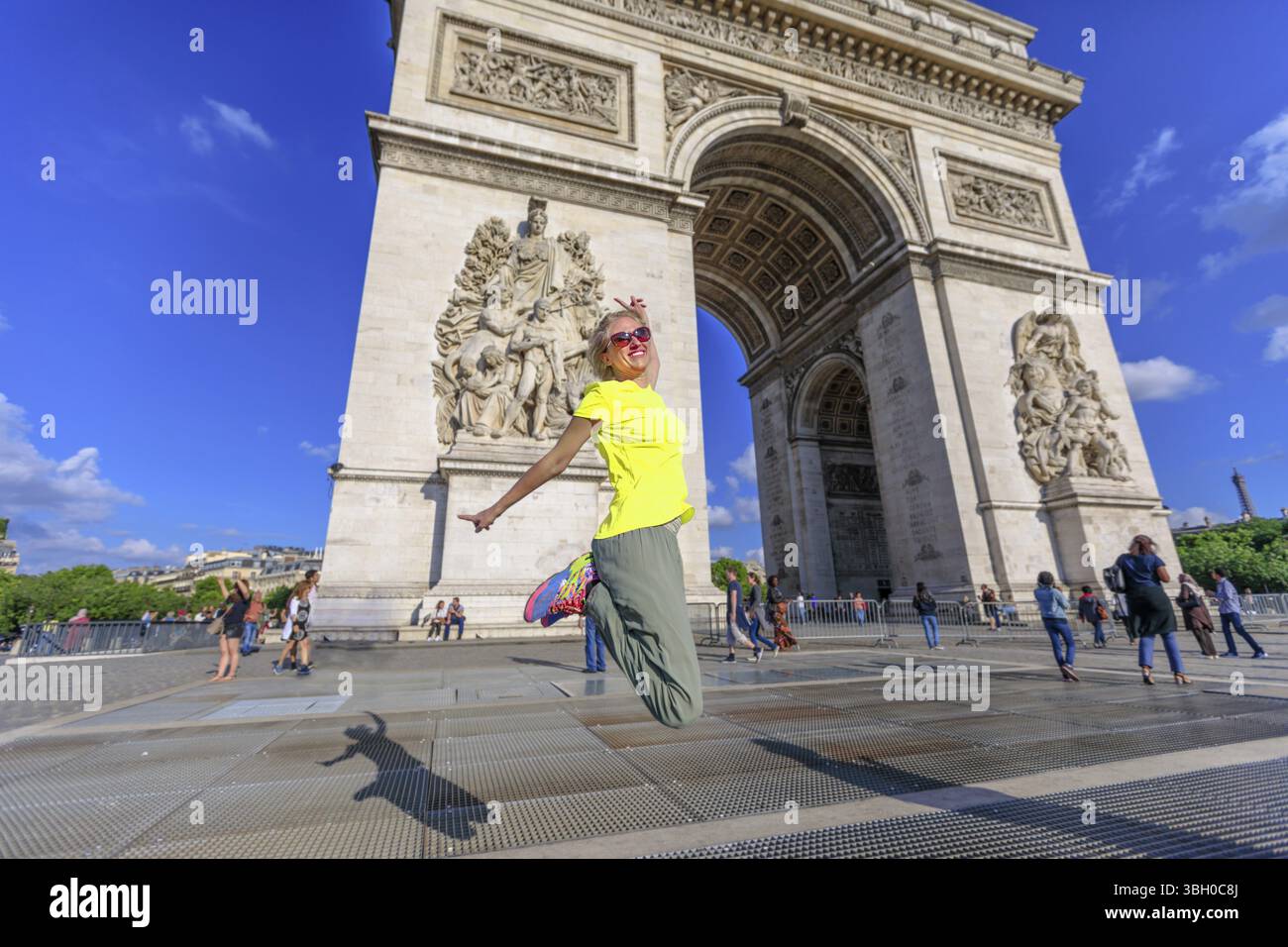 Frau mit gelber Weste, die beim Triumphbogen springt. Beliebtes Wahrzeichen in Paris, Frankreich. Glücksbegriff für den Sieg der Volksproteste. Weste Stockfoto