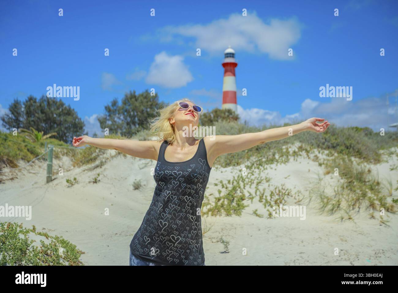 Sorglos Frau mit offenen Armen auf weißen Strand mit Dünen in Geraldton, Western Australia. Die historische Moore Lighthouse Point im Jahre 1878 gebaut, ist ein Symbol Stockfoto
