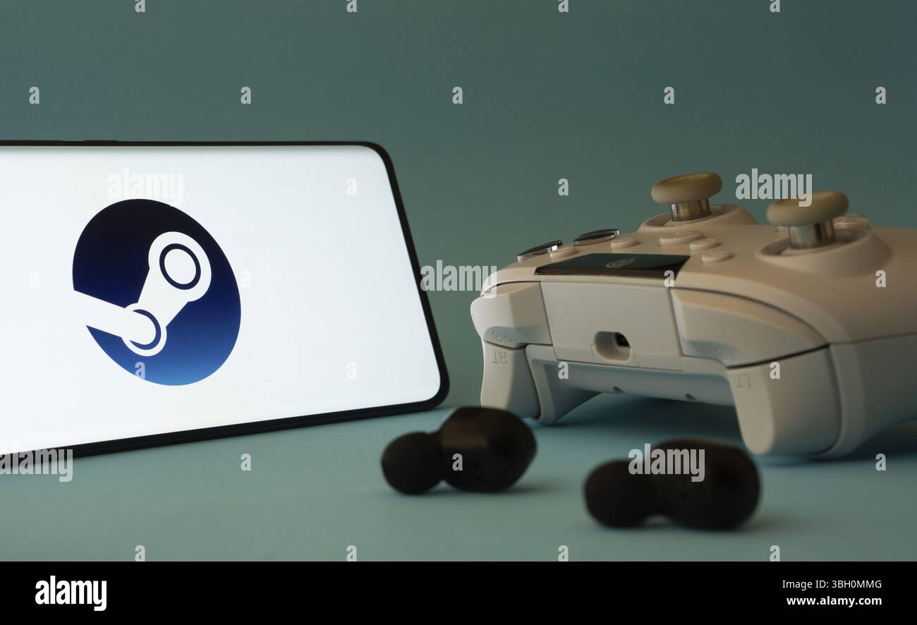Ein Smartphone mit einem Steam App-Symbol neben einem Controller und Ohrstöpseln auf einer blauen Oberfläche Stockfoto