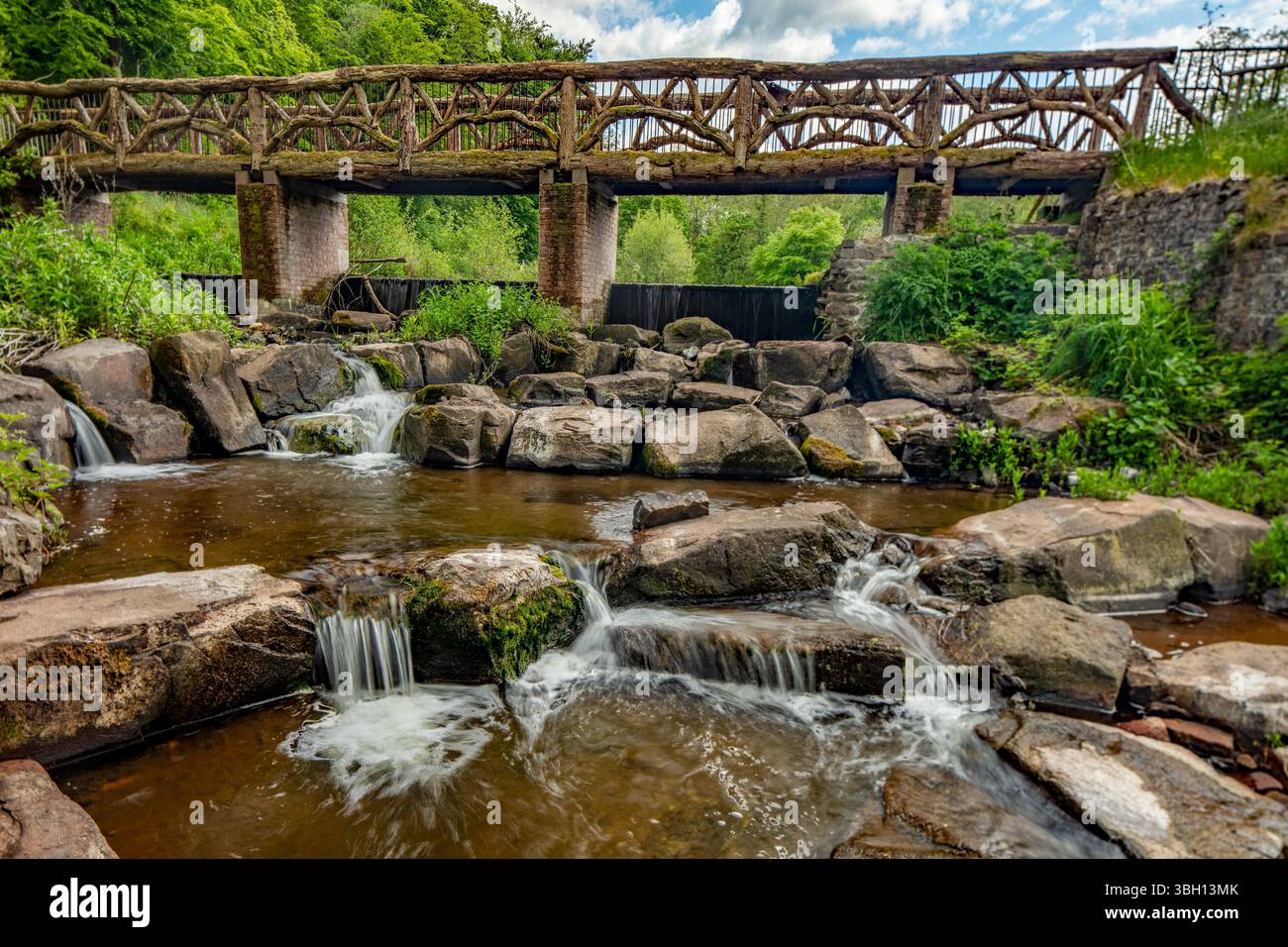 Die rustikale Oak Bridge im National Botanic Garden of Wales, Carmarthenshire, Wales, mit rauschendem Fluss Towi über Felsen im Vordergrund. Verlockend Stockfoto