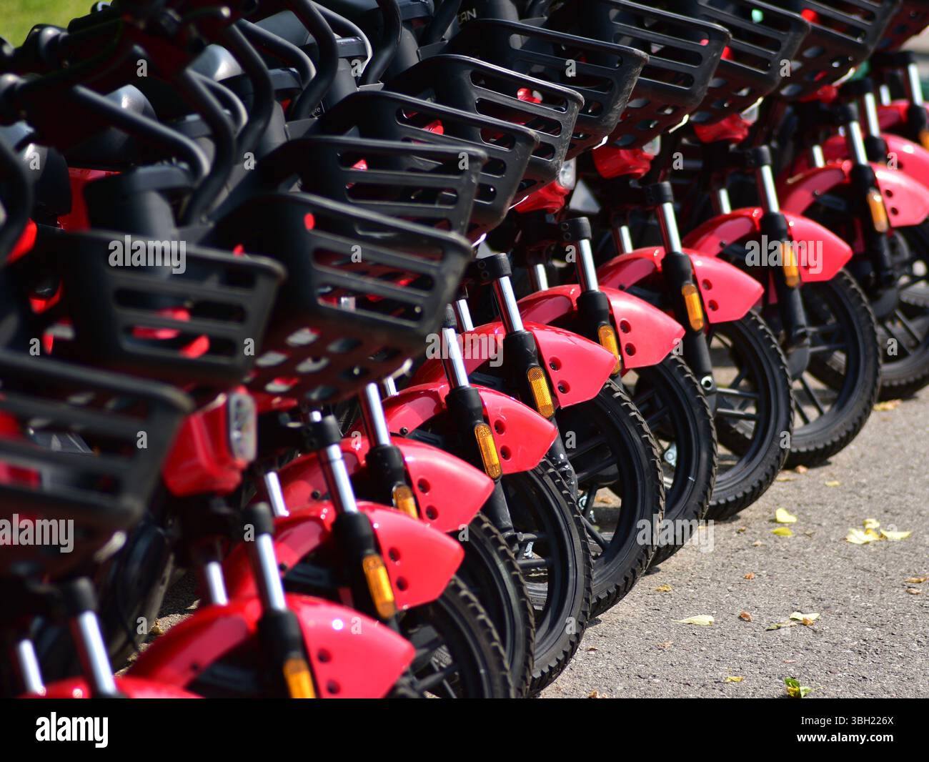 Reihe roter Elektromotorroller, die ordentlich am Straßenrand geparkt sind. Nachhaltiger Stadtverkehr, Mikromobilität und moderner städtischer Pendelverkehr mit Öko-Frie Stockfoto