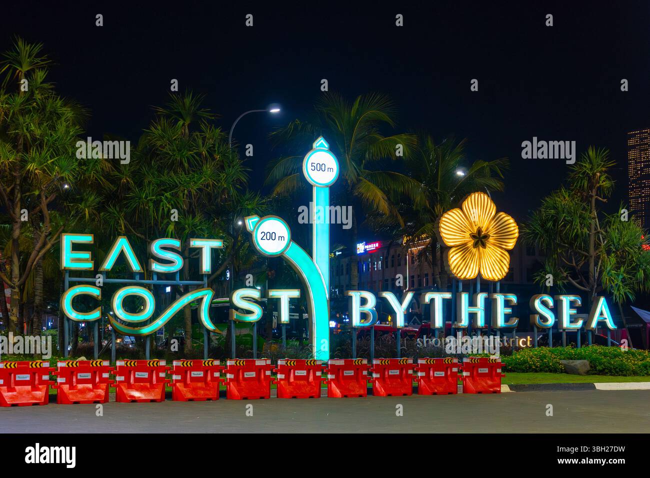 Schild mit der Aufschrift East Coast by the Sea bei Pantai Indah Kapuk (PIK). Das Schild leuchtet nachts auf. Vor dem Schild befinden sich mehrere rote Barrieren Stockfoto