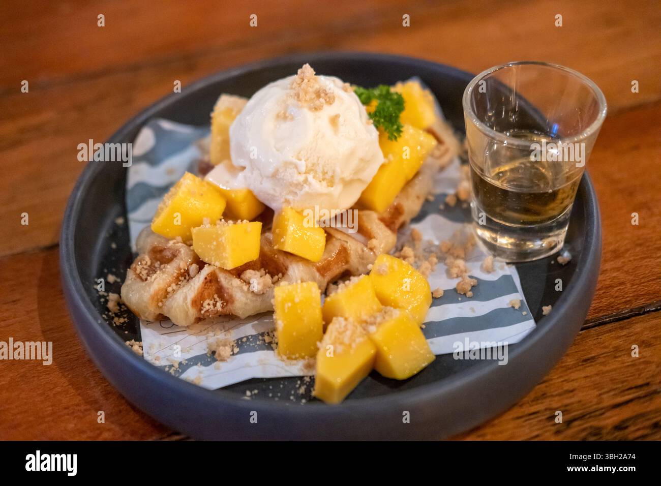 Croffle, eine Mischung aus Croissant und Waffel mit Mango, Eis und Honig, serviert auf einem Teller Stockfoto