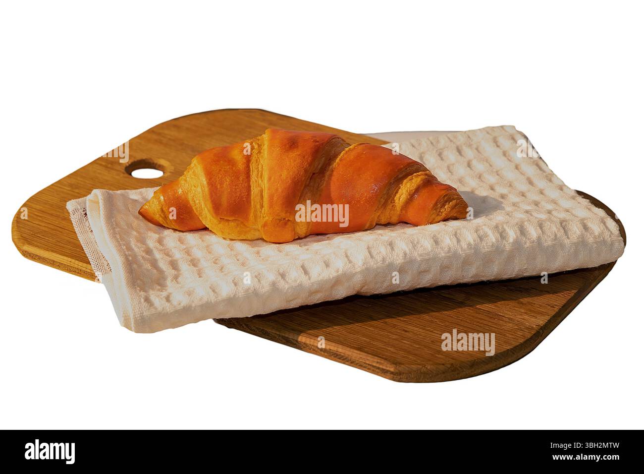 Frisches goldenes Croissant auf einem gefalteten weißen Handtuch auf einem hölzernen Schneidebrett. Leckeres Backfood-Konzept mit natürlichem warmem Licht und minimalistischem K Stockfoto